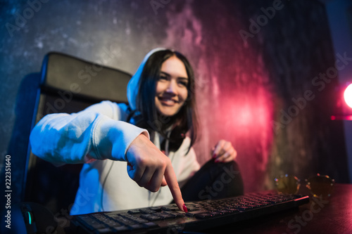 Woman in the hood sitting and working at laptop as hacker. Running malware program on computer in the internet with malevolent smile on her face. photo