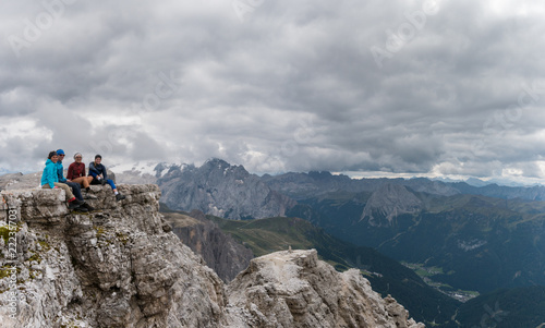 Billede på lærred four young male and female hikers sitting on a mountain peak ledge in the Dolomi