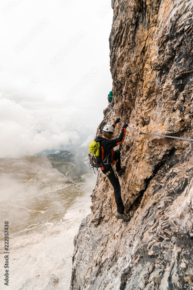 Obraz premium young attractive female university student on a vertical and exposed rock face climbs a Via Ferrata in Alta Badia in the South Tyrol