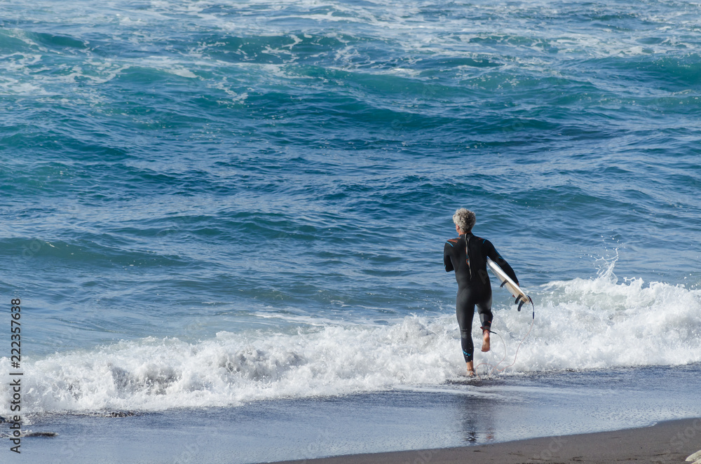 Hombre corriendo hacia el mar para hacer surf durante el atardecer en en la playa de El Socorro, Los Realejos. Isla de Tenerife, Islas Canarias. España. Hombre corriendo hacia el mar para hacer surf durante el atardecer en en la playa de El Socorro, Los Realejos. Isla de Tenerife, Islas Canarias. España.