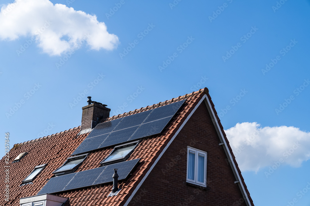 Roof with red roof tiles and solar panels for making renewable energy and a clear blue sky