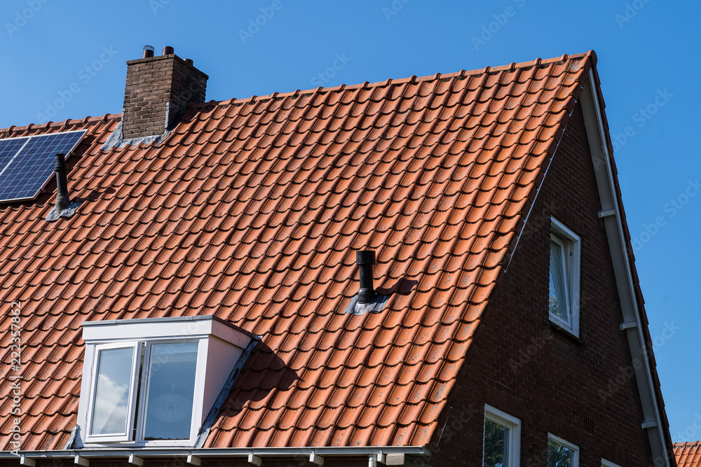 Roof with red roof tiles chimney and solar panels for making renewable energy and a clear blue sky