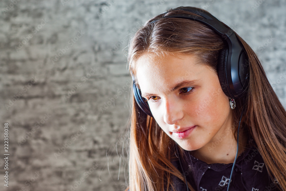 portrait of young teenager brunette girl with long hair listening music on headphones on gray wall background portrait of young teenager brunette girl with long hair listening music on headphones on gray wall background