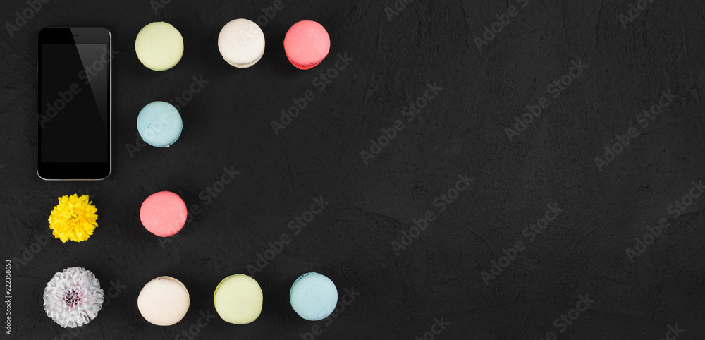 Tasty colorful macarons with phone and flowers on vintage stone background. Top view with copy space on the right Tasty colorful macarons with phone and flowers on vintage stone background. Top view with copy space on the right