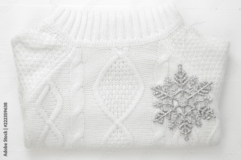 Obraz premium Knitted winter white sweater and snowflake decoration on white wooden background. top view