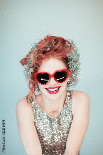 funny young lady in glitter outfit with red heart shape glasses portrait, christmas garland and red hair