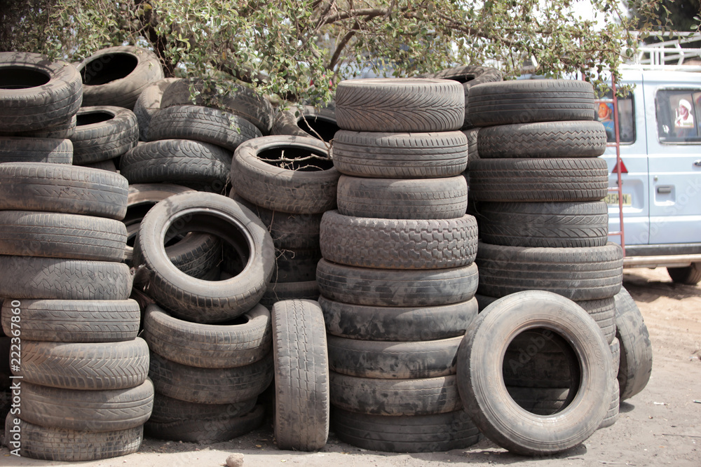 close up of a pile of used black dusty tires, outdoors, on street in the Gambia, with natural light with blue sky and green trees close up of a pile of used black dusty tires, outdoors, on street in the Gambia, with natural light with blue sky and green trees