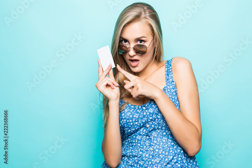 Smiling young woman in sunglasses hold credit card on blue background.