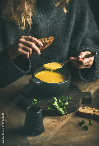 Woman in dark winter sweater eating sweet corn and shrimp chowder soup from black bowl with toasted bread, close-up. Autumn or winter warming food
