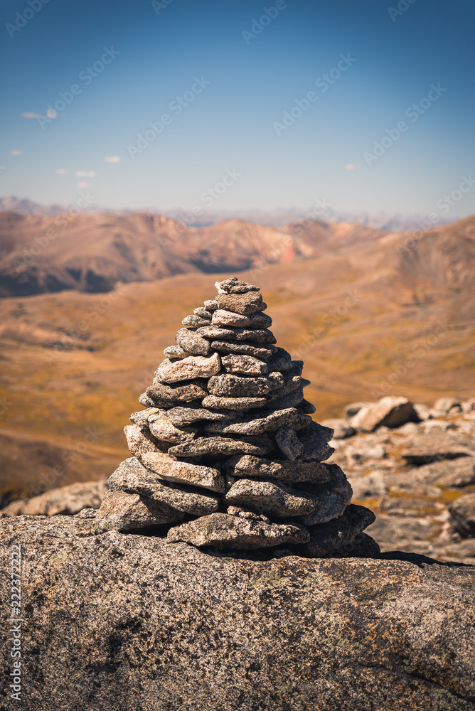 A large cairn marking a trail in Colorado with mountains in the background. 