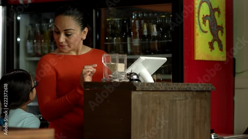 Beautiful Hispanic woman speaks joyfully with her daughter while working the front of house at their family owned Mexican restaurant