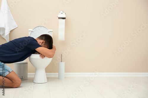 Fototapeta Naklejka Na Ścianę i Meble -  Young man vomiting in toilet bowl at home