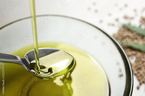 Pouring hemp oil into spoon over glass bowl  closeup