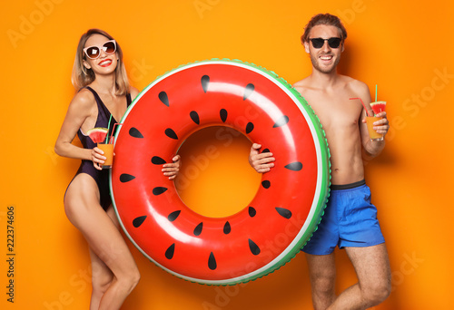 Happy young couple in beachwear with inflatable ring and cocktails on color background