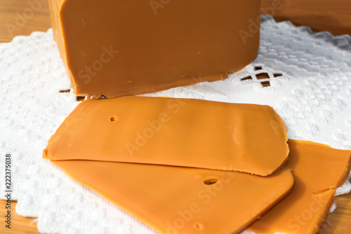 Traditional Norwegian brown cheese on a white napkin with embroidery hardanger. Brunost. Sheep cheese. A piece of soft brown caramel cheese on a wooden surface. photo