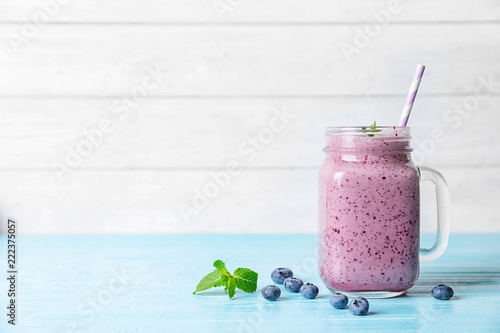 Tasty blueberry smoothie in mason jar on table against light background with space for text