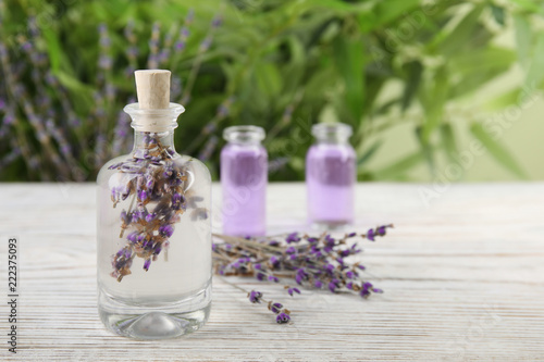 Fototapeta Naklejka Na Ścianę i Meble -  Bottle with natural herbal oil and lavender flowers on table against blurred background. Space for text