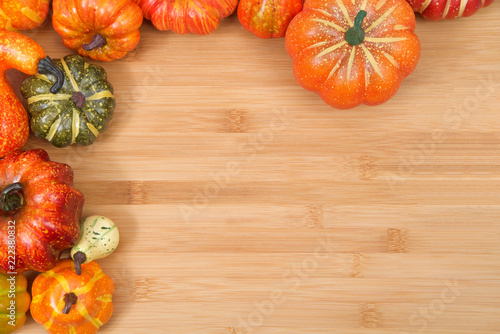 Close up on small pumpkins squash and gourds creating a half square frame around wood textured background with copy space.