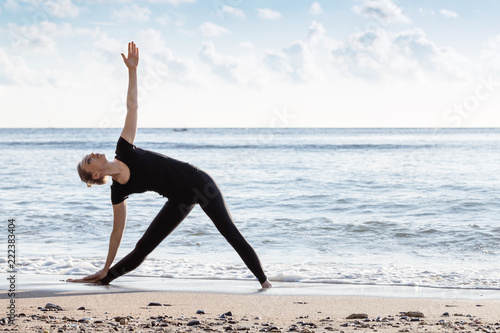 Young age woman in black doing yoga on sand beach
