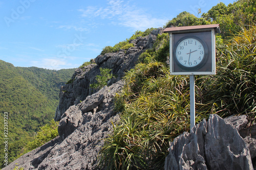 Clock on the top of limestone mountain with green nature and blue sky  background