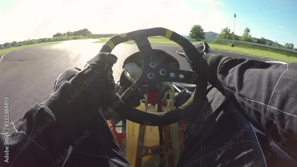 POV, LENS FLARE: Driving a go-kart in a black suit through sharp bends of a bumpy racetrack. Cinematic first person view of steering a go cart while racing in a fun competition on the sunny circuit.