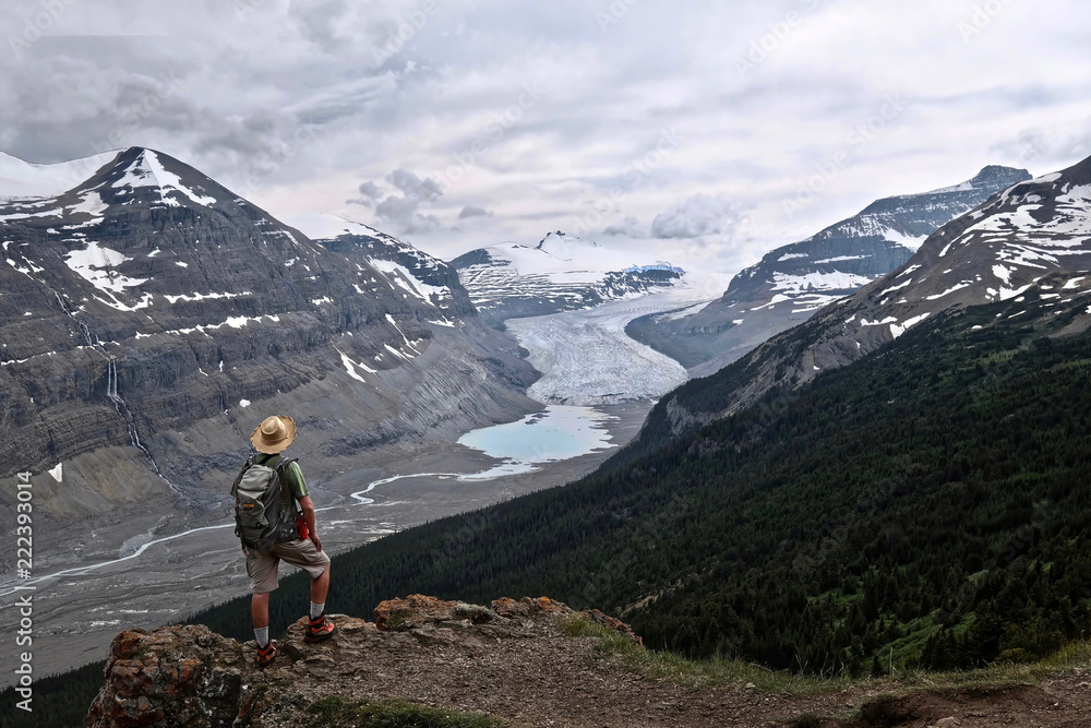 Man hiker on the steep cliff over Columbia Icefield glacier and a moraine lake. Summer storm in  Banff / Jasper National Park. Canadian Rocky Mountains.  Patterson Ridge trail. Alberta. Canada.