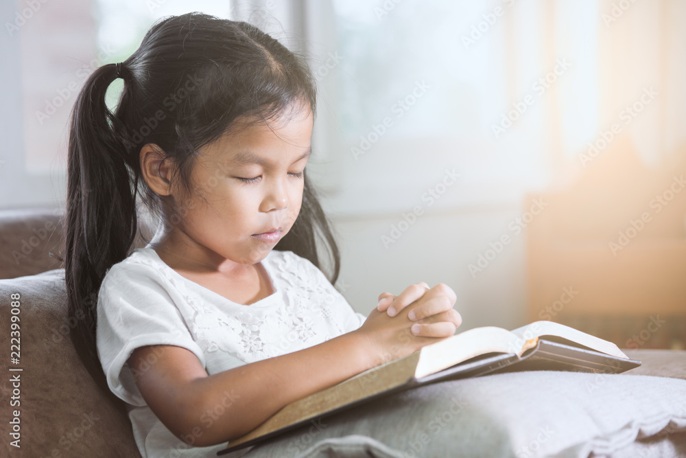 Cute asian little child girl closed her eyes and folded her hand in prayer on a Holy Bible for faith concept Cute asian little child girl closed her eyes and folded her hand in prayer on a Holy Bible for faith concept