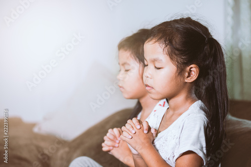 Cute asian child girl and her sister praying with folded her hand in the room together for faith spirituality and religion concept