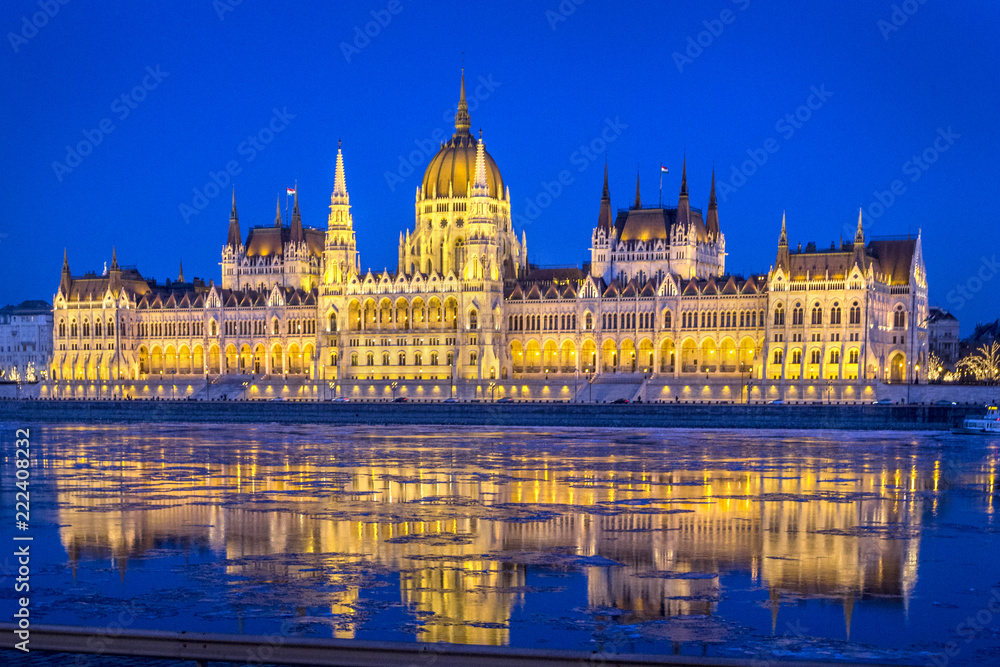 Night view of illuminated Hungarian Parliament Building is seat of National Assembly of Hungary with beautiful reflection during spring on ice drift Danube River, Budapest, Hungary.
