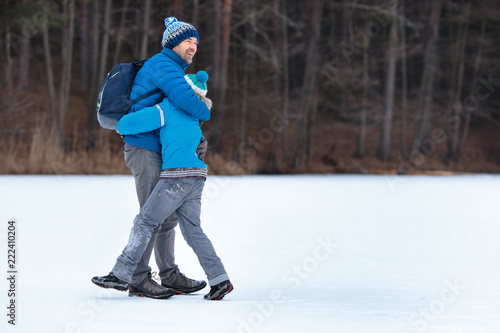 Cute cheerful boy and his father playing by winter lake