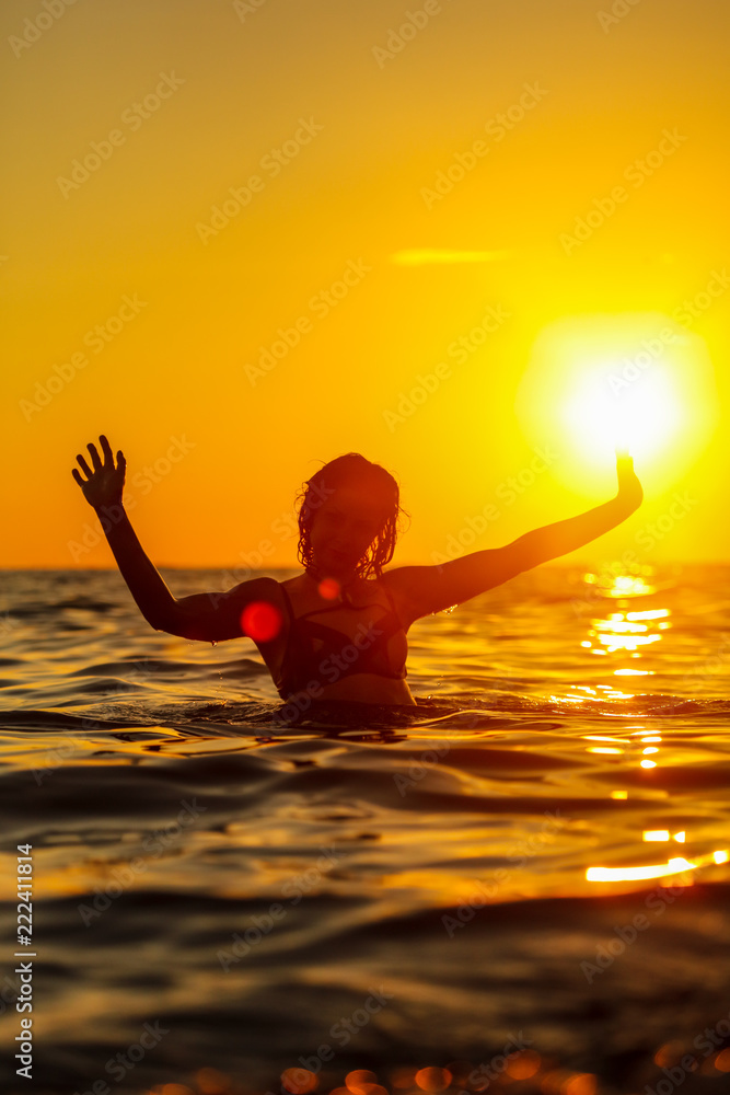 A girl is floating in the sea at sunset