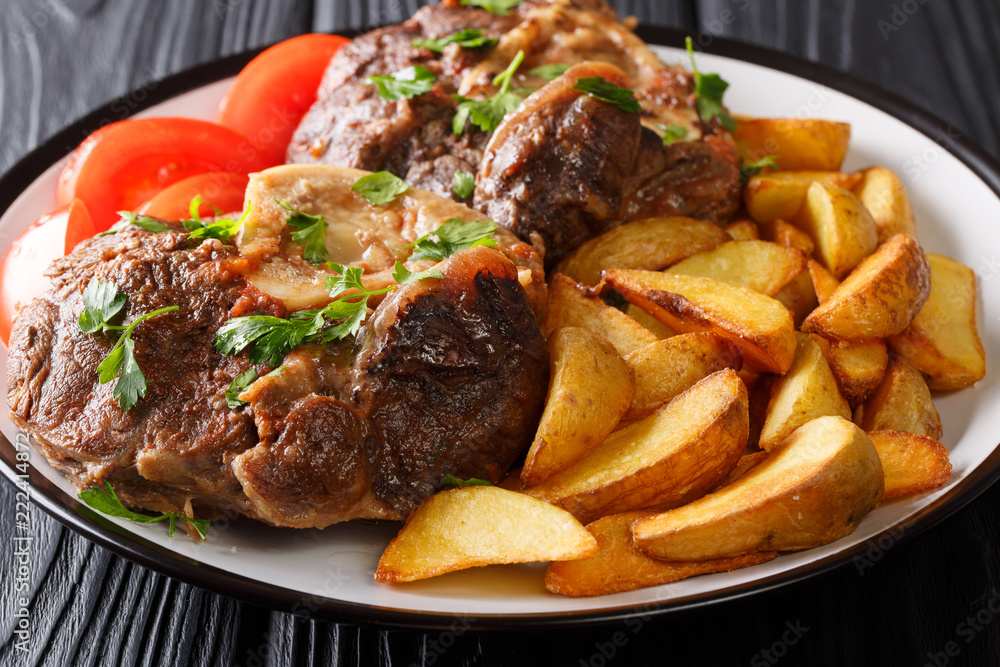 Spicy steak Ossobuco with fried potato wedges and tomatoes close-up on a plate. horizontal Spicy steak Ossobuco with fried potato wedges and tomatoes close-up on a plate. horizontal