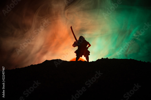 Fighter with a sword silhouette a sky ninja. Samurai on top of mountain with dark toned foggy background.