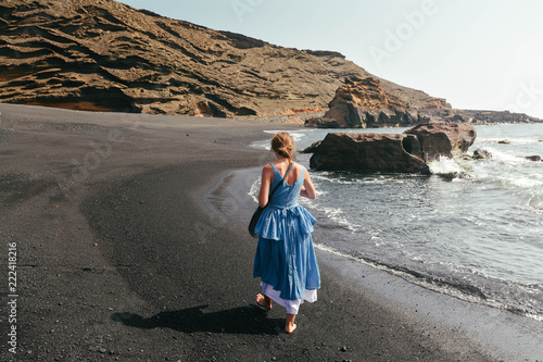 Girl walking on fantastic sea black beach in Spain. Photo with added film and grain filter. Back view