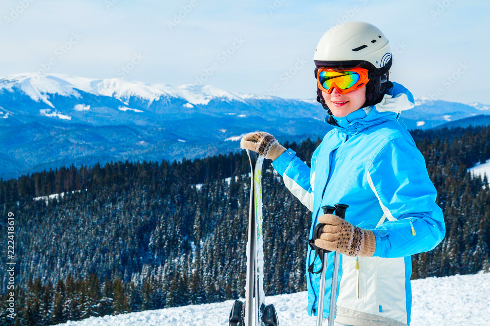 a woman in a blue suit, a helmet and glasses is standing with skis on top of a mountain