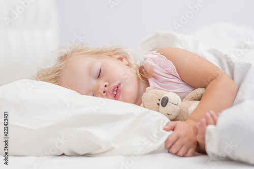 little baby girl sleeping on a bed with toy bear