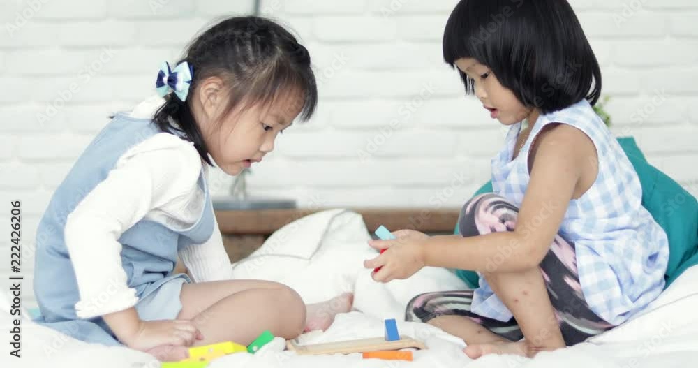 Two little asian cute girl playing colourful wood block on bed together . Two little asian cute girl playing colourful wood block on bed together .