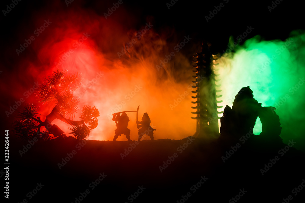 Fototapeta premium Samurai fighting concept. Silhouette of samurais in duel near tree and old temple. Picture with two samurais and sunset sky. Selective focus