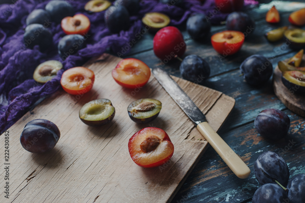 Fresh organic plums and plum slices on wooden board and rustic wooden table, autumn harvest, seasonal fruits, healthy lifestyle, top view, selective focus Fresh organic plums and plum slices on wooden board and rustic wooden table, autumn harvest, seasonal fruits, healthy lifestyle, top view, selective focus