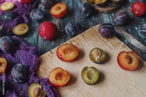 Fresh organic plums and plum slices on wooden board and rustic wooden table, autumn harvest, seasonal fruits, healthy lifestyle, selective focus