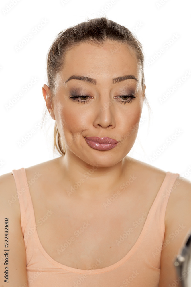 Young bored woman looking in the mirror on white background Young bored woman looking in the mirror on white background