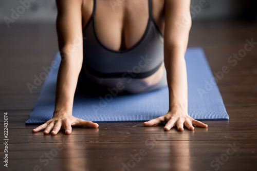 Sporty woman practicing yoga, doing variation of Cobra exercise, Bhujangasana, pose for flexible shoulders, working out, wearing sportswear, grey top, indoor close up, yoga studio