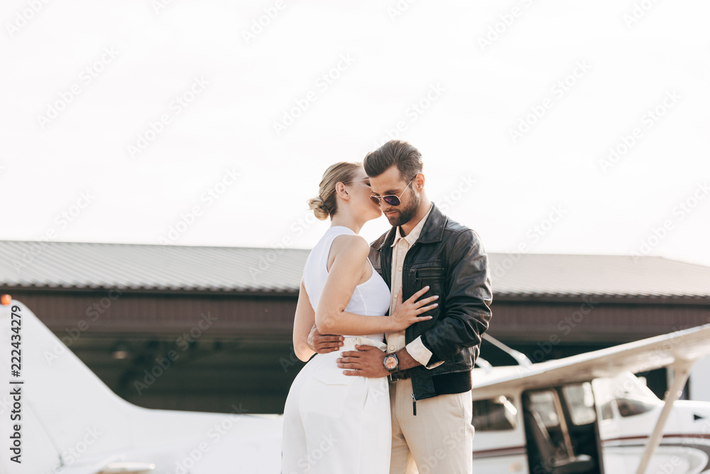attractive young woman whispering on ear to boyfriend near plane attractive young woman whispering on ear to boyfriend near plane
