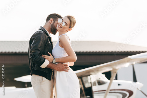 selective focus of fashionable man in leather jacket embracing attractive girlfriend near plane © LIGHTFIELD STUDIOS
