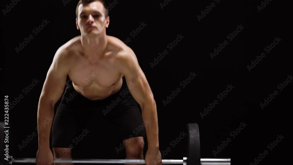Man is doing exercises with a barbell, is engaged in a crossfit on a black background in the studio Man is doing exercises with a barbell, is engaged in a crossfit on a black background in the studio