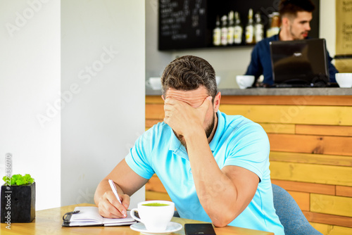 Man disappointed desperate face sit cafe with mug of coffee and notepad. Headache and stress. Deadline coming search ideas need inspiration. Crisis in creativity and inspiration. Man suffers headache