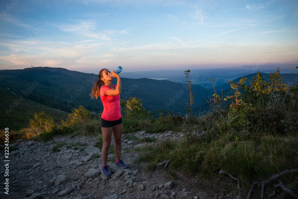 Woman trail runner drinking water from the plastic bottle
