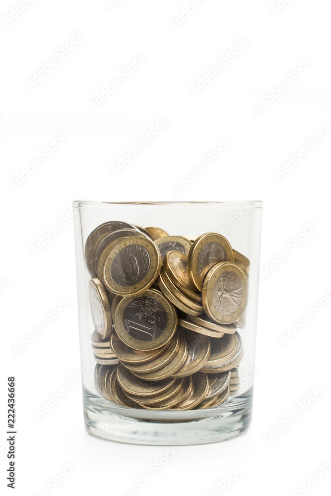 Monedas dentro de un vaso hucha de cristal sobre fondo blanco aislado. Vista de frente y de cerca. Concepto ahorro. Copy space. Formato vertical Monedas dentro de un vaso hucha de cristal sobre fondo blanco aislado. Vista de frente y de cerca. Concepto ahorro. Copy space. Formato vertical