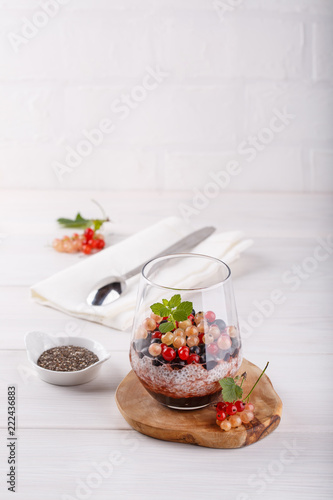 Chia pudding with fresh currant berries in glass on white table.
