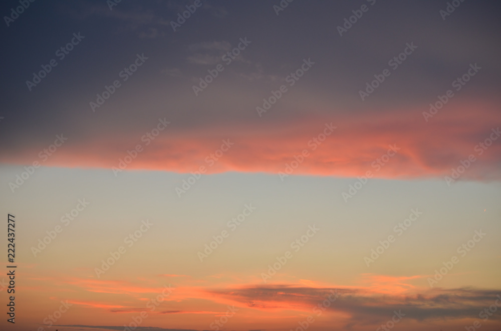 Cloudscape in dusk with clouds in grey, violet and orange colors and blue sky - suitable for a background